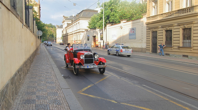 19 - A red vintage-style sightseeing tour car driving down a cobblestone street in Prague